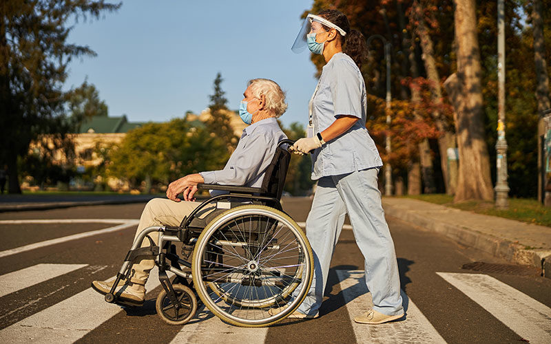 A care worker pushing an elderly man in a wheelchair.