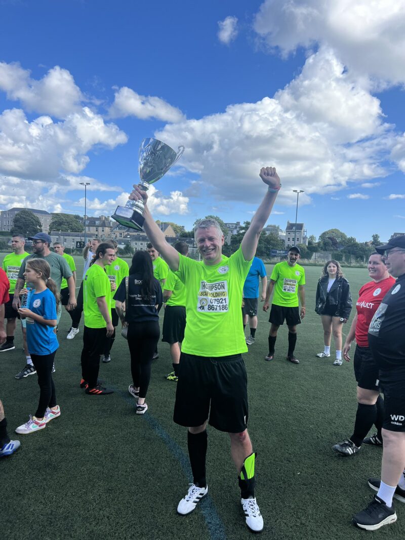 Luke MP wearing a green football shirt lifting a trophy